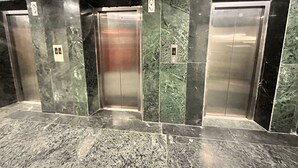 Three elevator doors in a lobby with marble flooring and walls. - Hotel Flamingo (Gurugram)