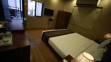 Una habitación de hotel con cama, mesita de noche, lámpara, armario y televisión en la pared.