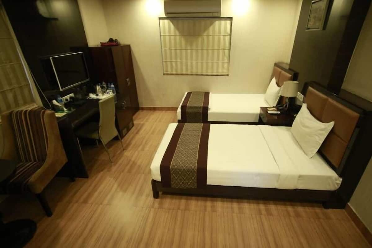 Una habitación de hotel con dos camas individuales, un escritorio con silla, televisor y armario.