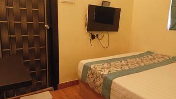 Una habitación con puerta de madera, una cama con cubrecama floral, un escritorio con silla y un televisor montado.