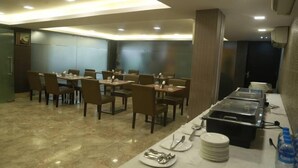 A dining area with tables and chairs, a buffet line, and a water dispenser. - Hotel Comfotel (Kolkata)