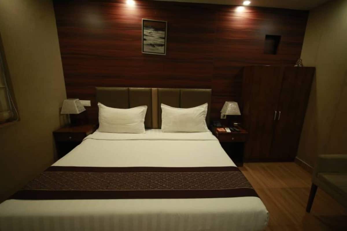 Una habitación de hotel con una cama grande, dos mesitas de noche con lámparas, un cabecero y un armario.