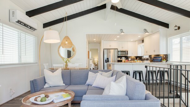 Un salon moderne avec un canapé d’angle gris, une table basse ronde sur laquelle se trouve une assiette de nourriture et un luminaire suspendu.