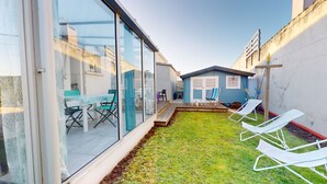 Un pati exterior modern amb parets de vidre, una petita terrassa i una zona enjardinada amb gandules.