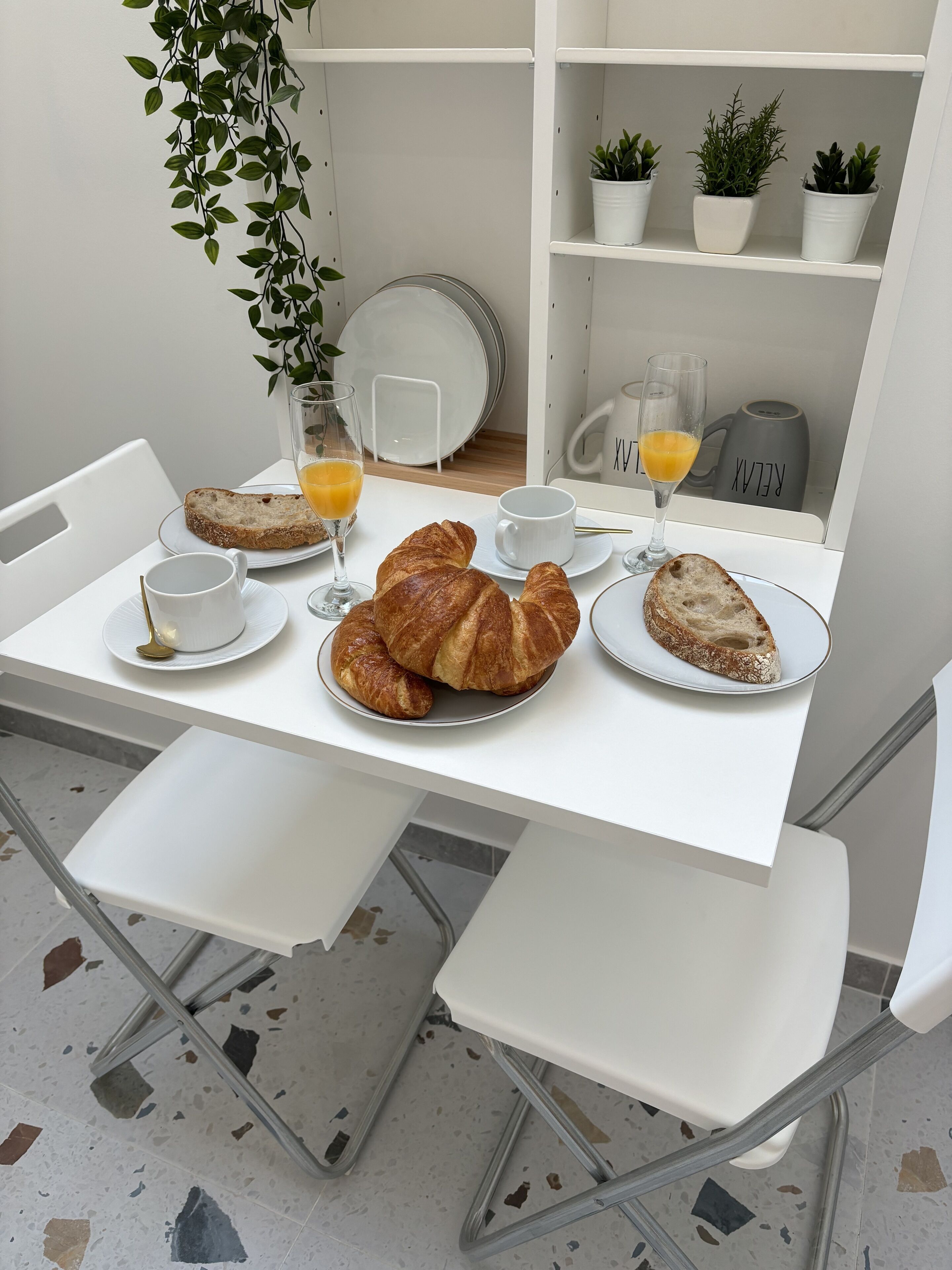 A breakfast table with croissants, orange juice, and a coffee mug.
