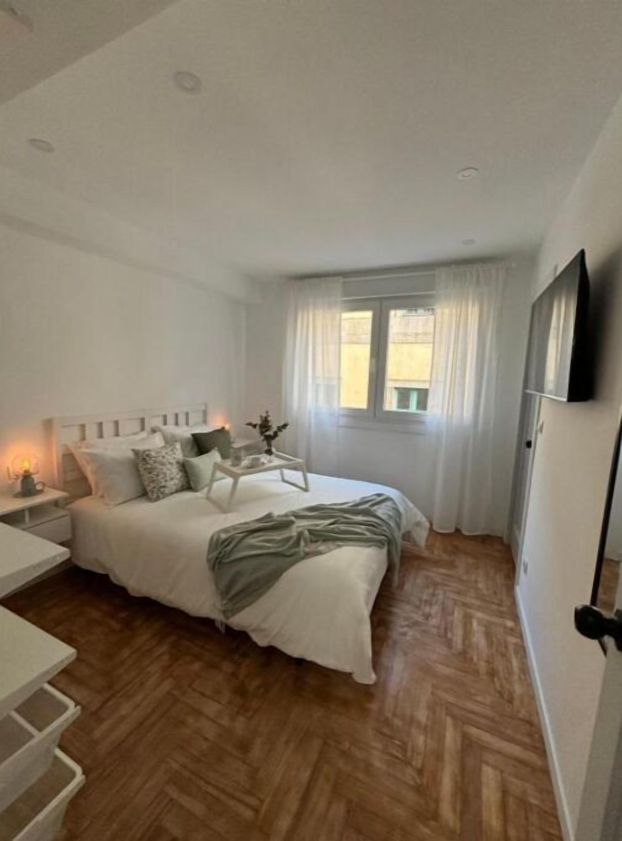 A bedroom with a bed, bedside table, lamp, and a window with curtains.