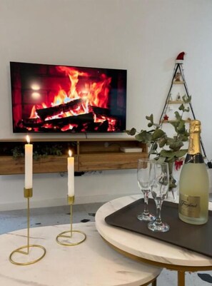 Une pièce chaleureuse avec une cheminée, des bougies, des verres et une bouteille de champagne sur une table.