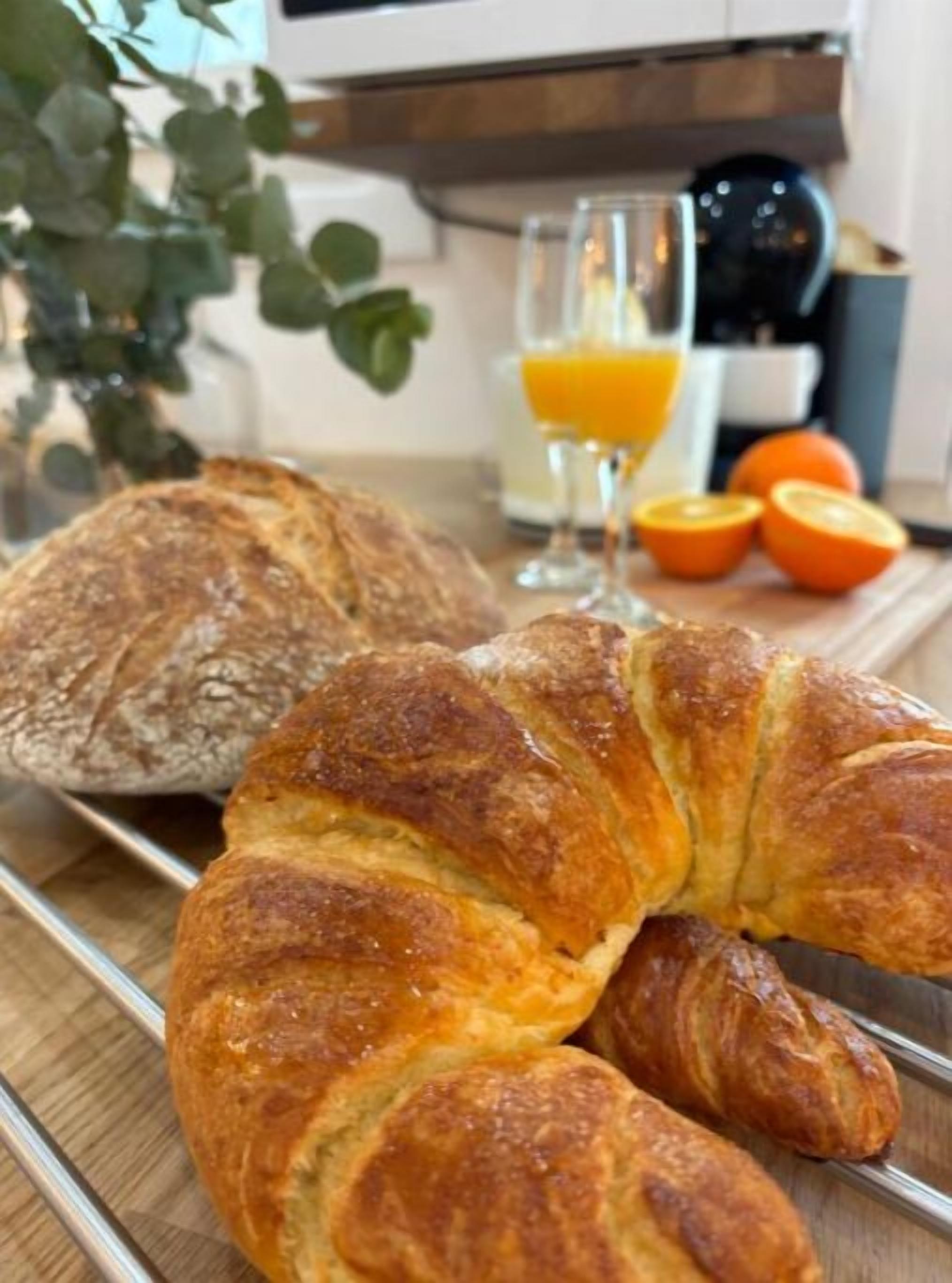 Un desayuno con un croissant, una barra de pan, un vaso de zumo de naranja y algunas naranjas sobre una bandeja.