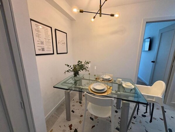 Un comedor con una mesa de vidrio, sillas blancas y un candelabro.