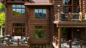 Une cabane en rondins dotée de nombreuses fenêtres, d’un balcon et d’un espace salon extérieur.