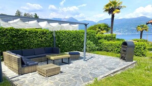 Un espace extérieur aménagé avec un canapé, deux petites tables d’appoint et un banc, entouré d’un sol en pierre et de verdure.