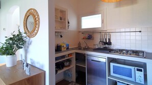 Une cuisine compacte avec des meubles blancs, un four à micro-ondes encastré, une cuisinière à gaz et un porte-ustensiles suspendu.