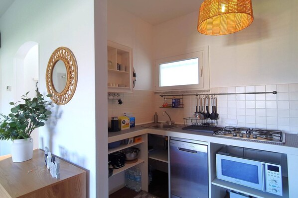 A compact kitchen with white cabinets, a built-in microwave, a gas stove, and a hanging rack for utensils.