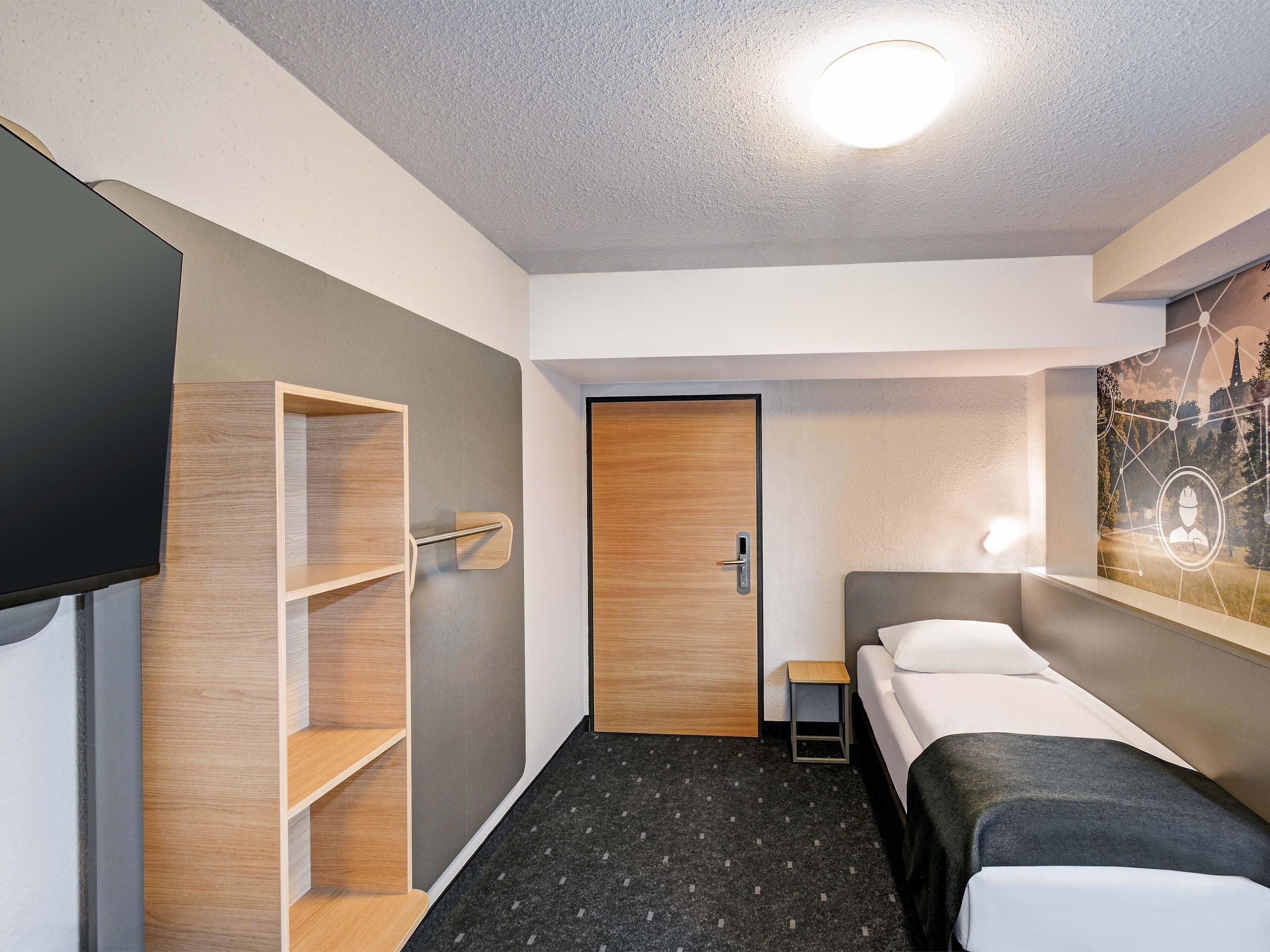 Een hotelkamer met een bed, een televisie, een houten wandplank en een deur.