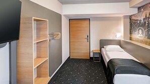 Een hotelkamer met een bed, een televisie, een houten wandplank en een deur.