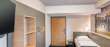 Una habitación de hotel con una cama, un televisor, una estantería de madera y una puerta.