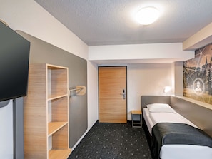 Una habitación de hotel con una cama, un televisor, una estantería de madera y una puerta.