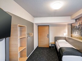 Una habitación de hotel con una cama, un televisor, una estantería de madera y una puerta.