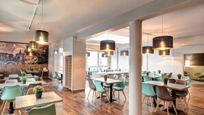 Un interior de restaurante moderno con suelo de madera, sillas verdes e iluminación colgante.