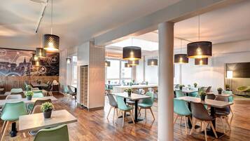 Een modern restaurantinterieur met houten vloeren, groene stoelen en hanglampen.