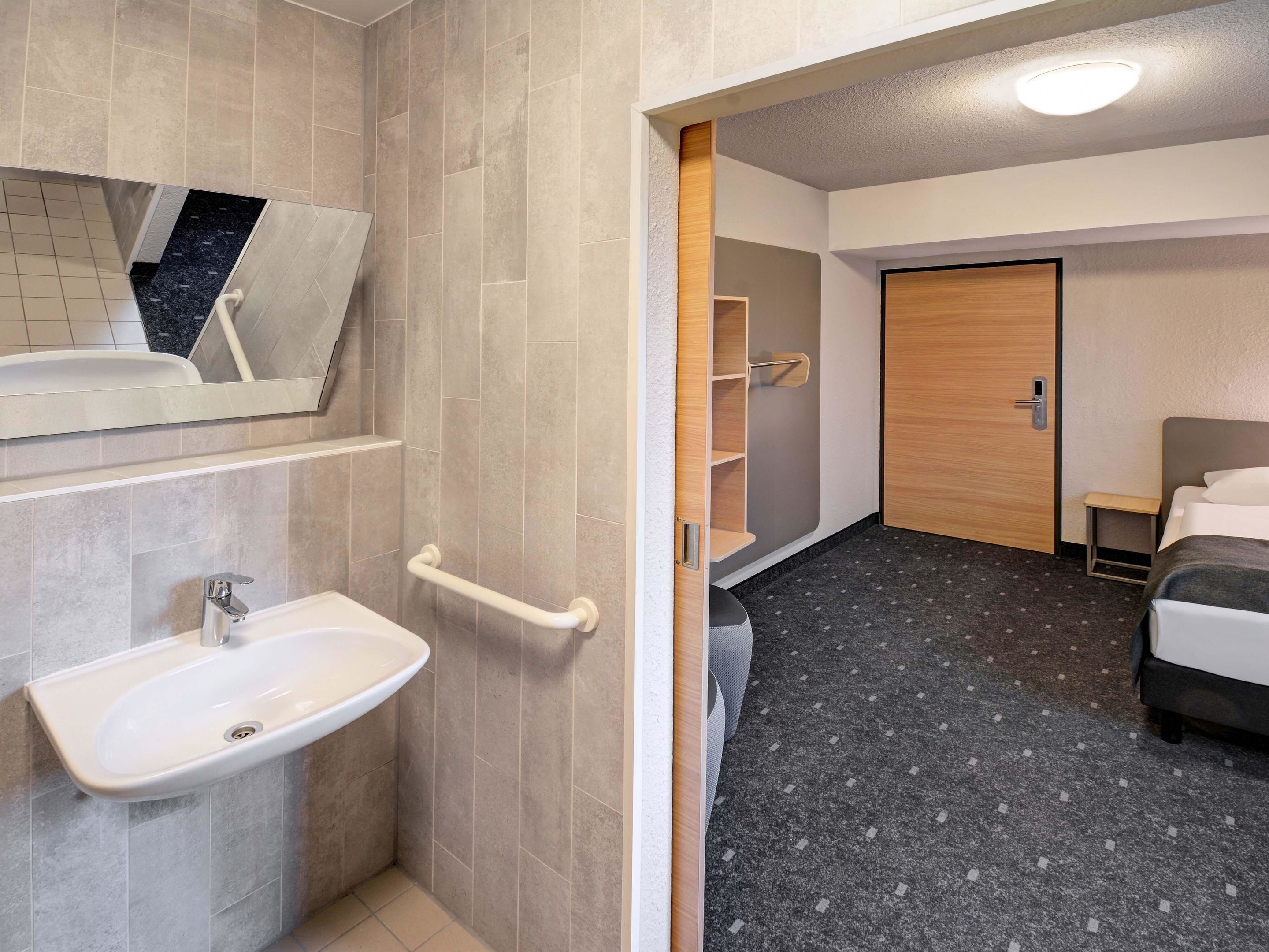 Une salle de bain moderne équipée d’un lavabo, d’un miroir et de barres d’appui.