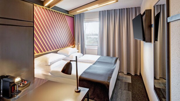 Habitación de hotel moderna con una cama, mesita de noche y televisor montado en la pared.
