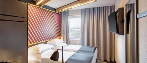 A modern hotel room with a bed, bedside table, and a TV mounted on the wall.