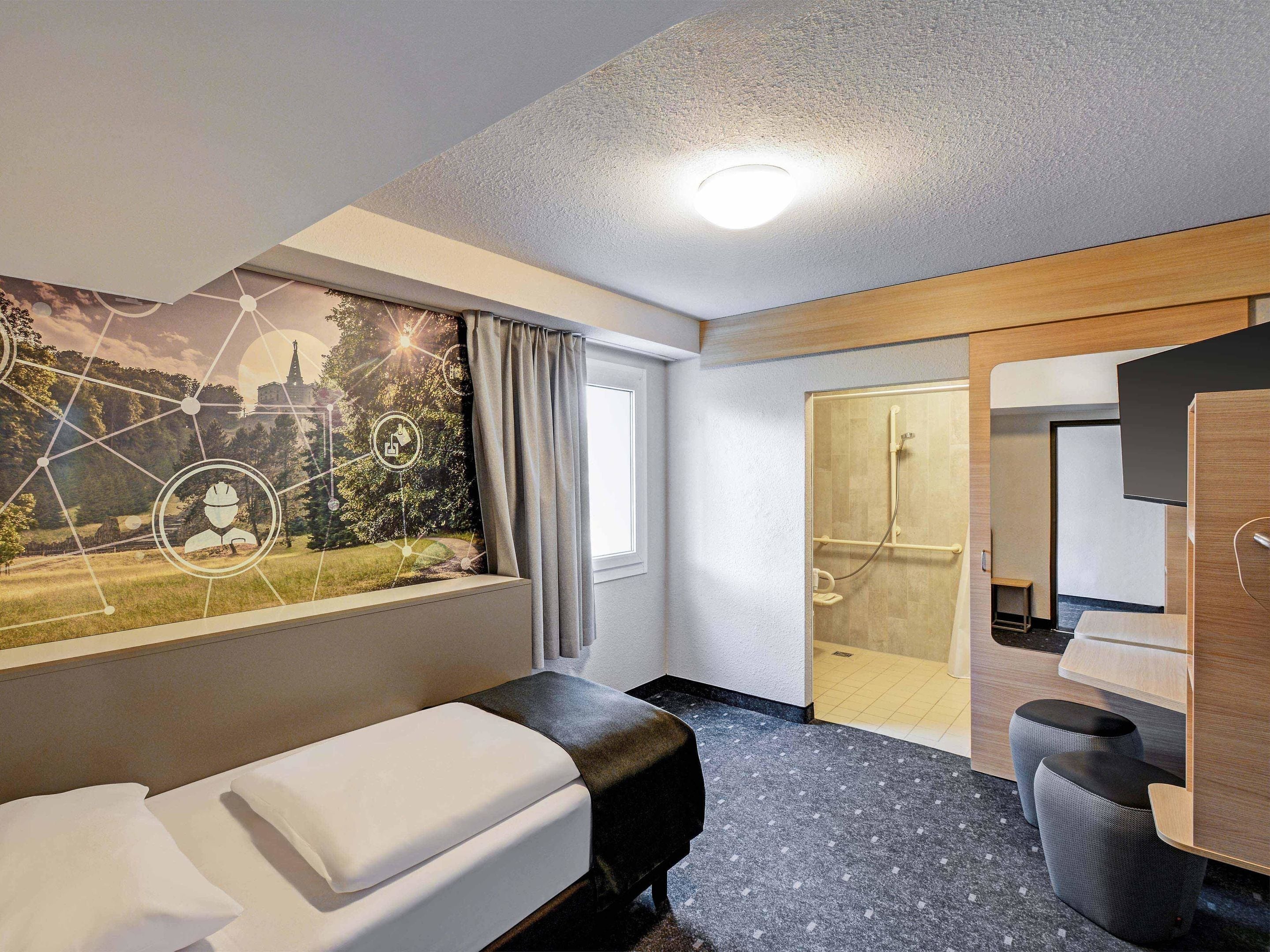 A hotel room with a bed, a shower area, and a large window with a view of a landscape.