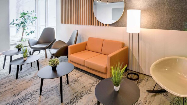 Een moderne zithoek met een bank, stoelen, een ronde tafel en een vloerlamp.