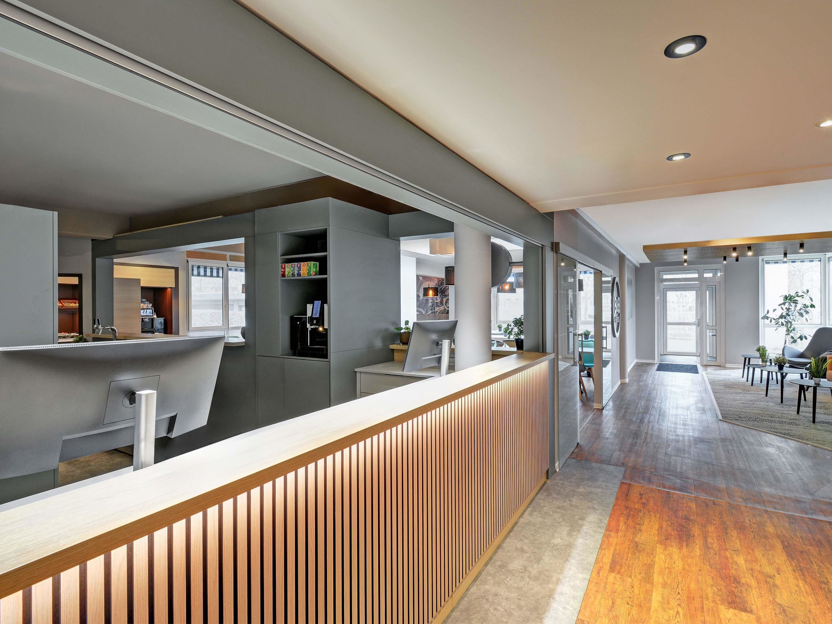 Een moderne receptiebalie met een houten toonbank, een glazen scheidingswand en uitzicht op de lobby.