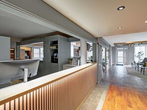 Un espace d’accueil moderne, doté d’un comptoir de réception en bois, d’une cloison en verre et offrant une vue sur le hall d’entrée.