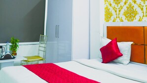 A hotel room with a bed, a desk, a chair, a wardrobe, and a ceiling fan. - Roomshala 124 Royal inn Rohini (New Delhi)
