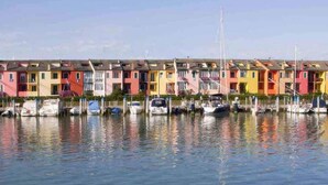 Fileira de casas coloridas à beira de um cais tranquilo, com barcos atracados à frente.