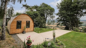 A wooden cabin with a sloped roof, a small porch, and a view of the surrounding landscape. - The Pod (Shrewsbury)