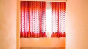 A room with a ceiling fan, red patterned curtains, and a shiny tiled floor. - Roomshala 041 Hotel Sky Residency (New Delhi)