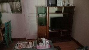 Un salon avec une table basse sur laquelle se trouvent des tasses et une boîte, un téléviseur et un fauteuil vert.