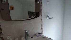 Une salle de bain avec un lavabo blanc, un miroir, des toilettes et une poubelle.