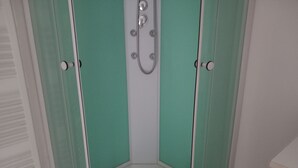 Un receveur de douche d’angle avec une porte en verre et un intérieur blanc.