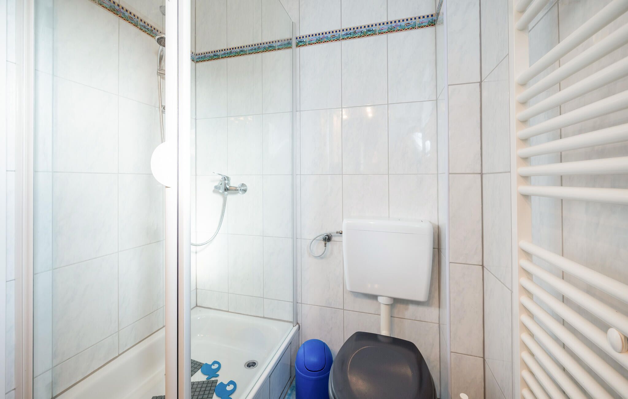 A bathroom with a glass shower enclosure, a bathtub, a toilet, and a hand dryer.