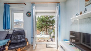 Un salon confortable avec un fauteuil en cuir, un téléviseur et une vue sur la terrasse extérieure.