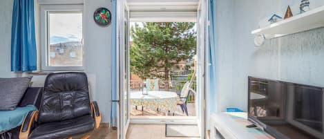 Uma sala de estar aconchegante com uma poltrona de couro, uma televisão e vista para o pátio externo.