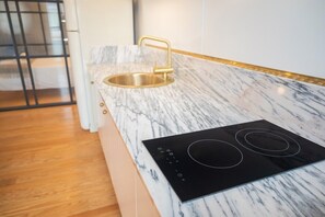 A modern kitchen with a marble countertop, a gold faucet, and a black induction cooktop.