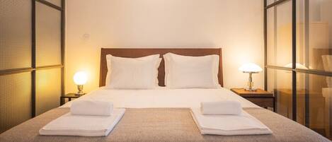A hotel room with a large bed, two bedside tables, and a window with a view.
