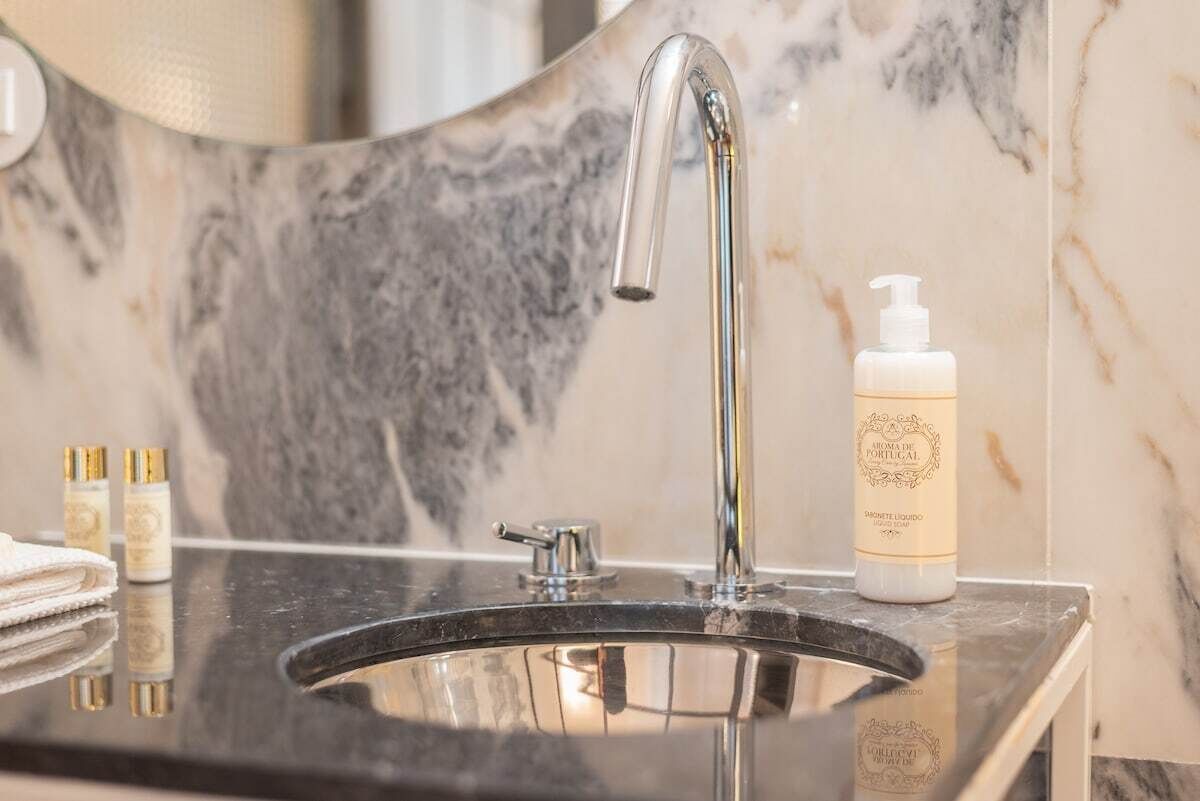 Une salle de bain avec un lavabo en marbre, un robinet moderne et un flacon de parfum portugais.