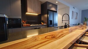 A modern kitchen with a wooden island, stainless steel appliances, and a large window providing a view of the city. - New apartment, spectacular views day and night. Close to everything!! (Surfers Paradise)