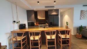 A modern kitchen with a central island, bar stools, and a grey sofa in the living area. - New apartment, spectacular views day and night. Close to everything!! (Surfers Paradise)