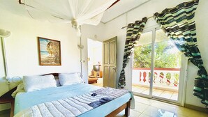 A bedroom with a bed, a television, and a balcony with curtains. - Régina Lodge (Antsiranana)
