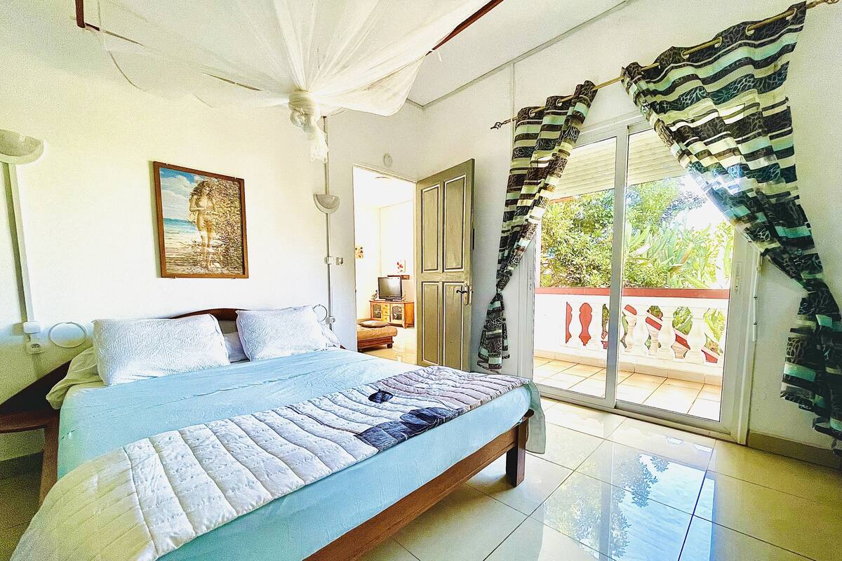 A bedroom with a bed, a television, and a balcony with curtains.
