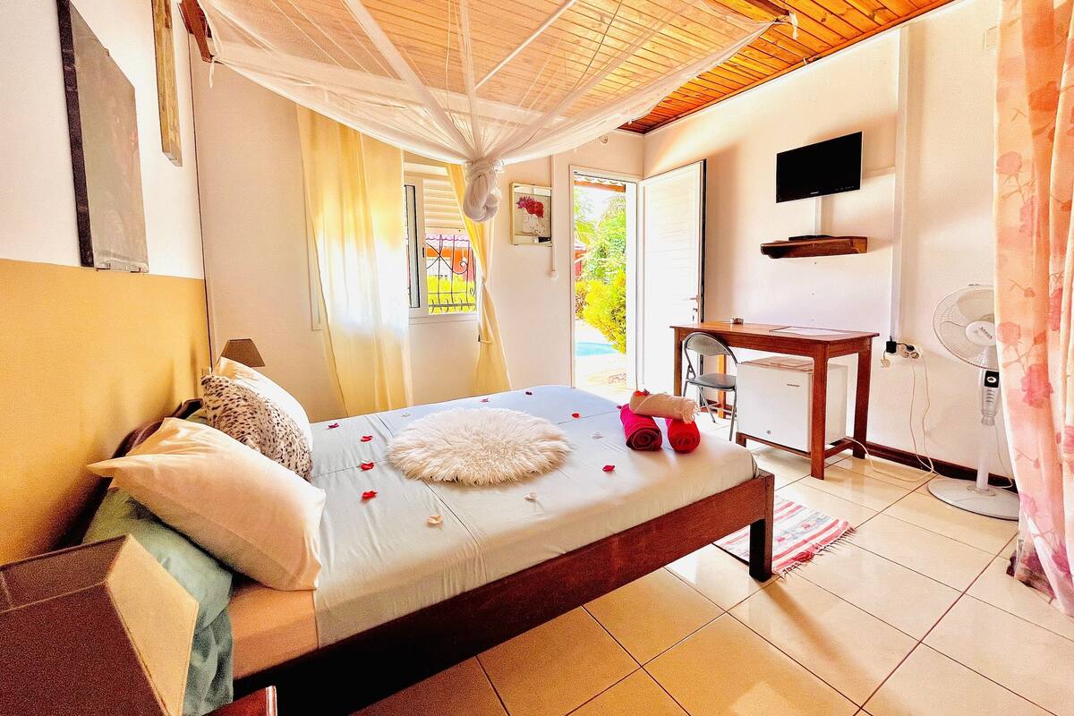 A bedroom with a bed, a desk, a chair, a TV, and a window with curtains.