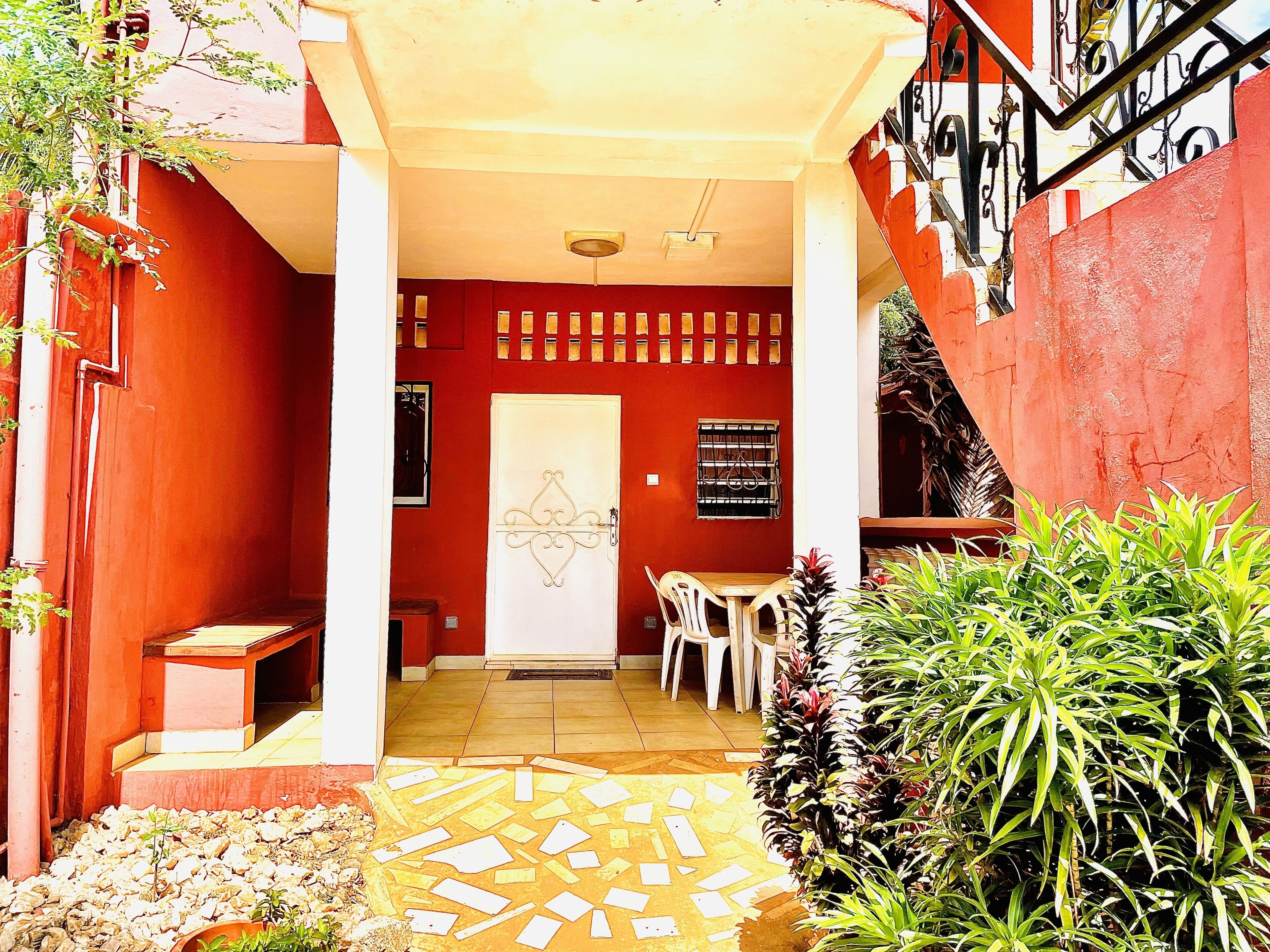 A red building with a white door, a tiled patio, and a staircase.